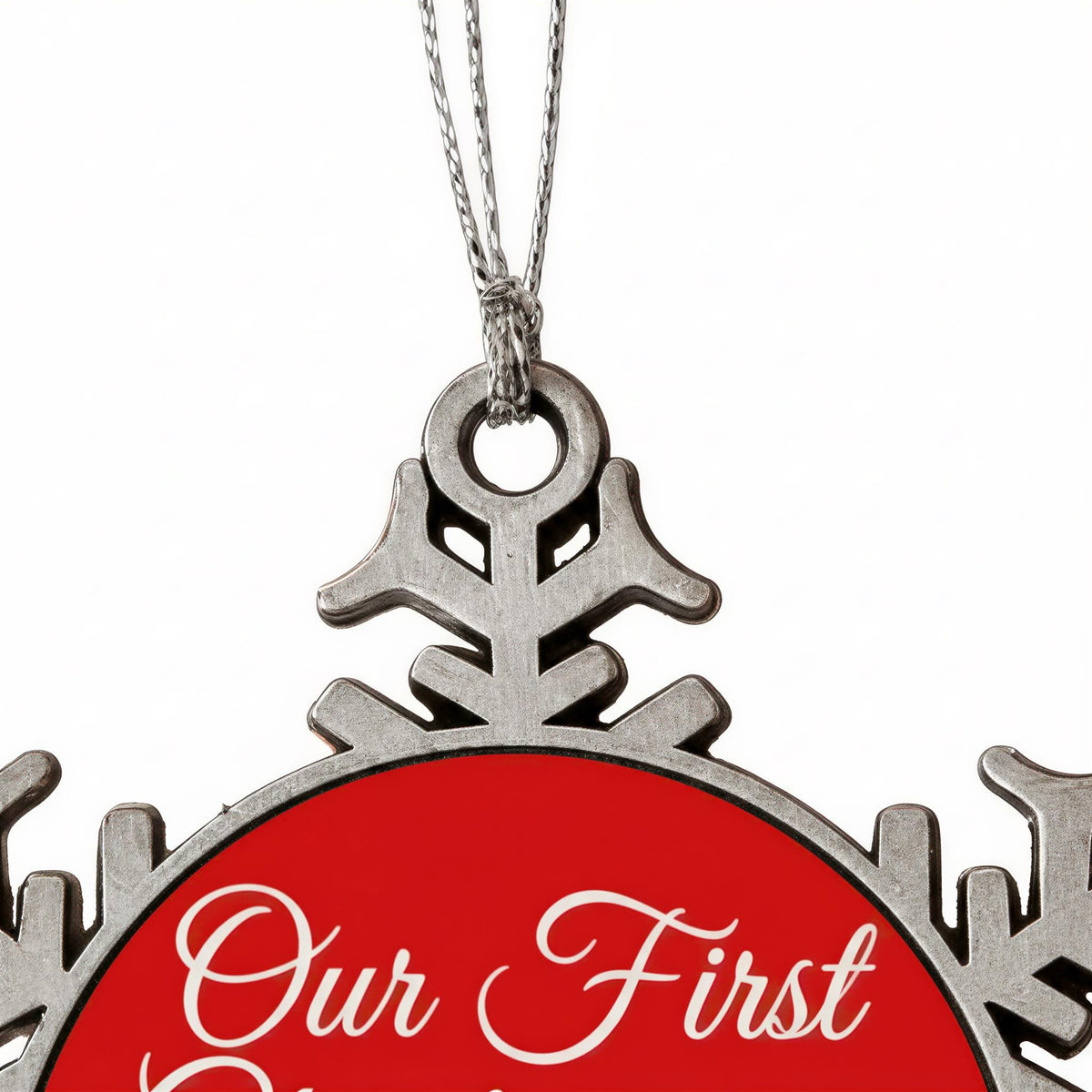 A close-up view of a red ornament with the text "Our First" written on it, hanging from a silver chain.