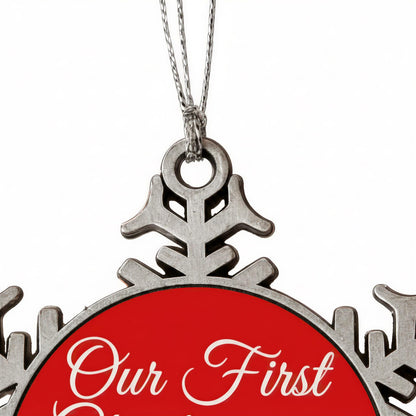 A close-up view of a red ornament with the text "Our First" written on it, hanging from a silver chain.