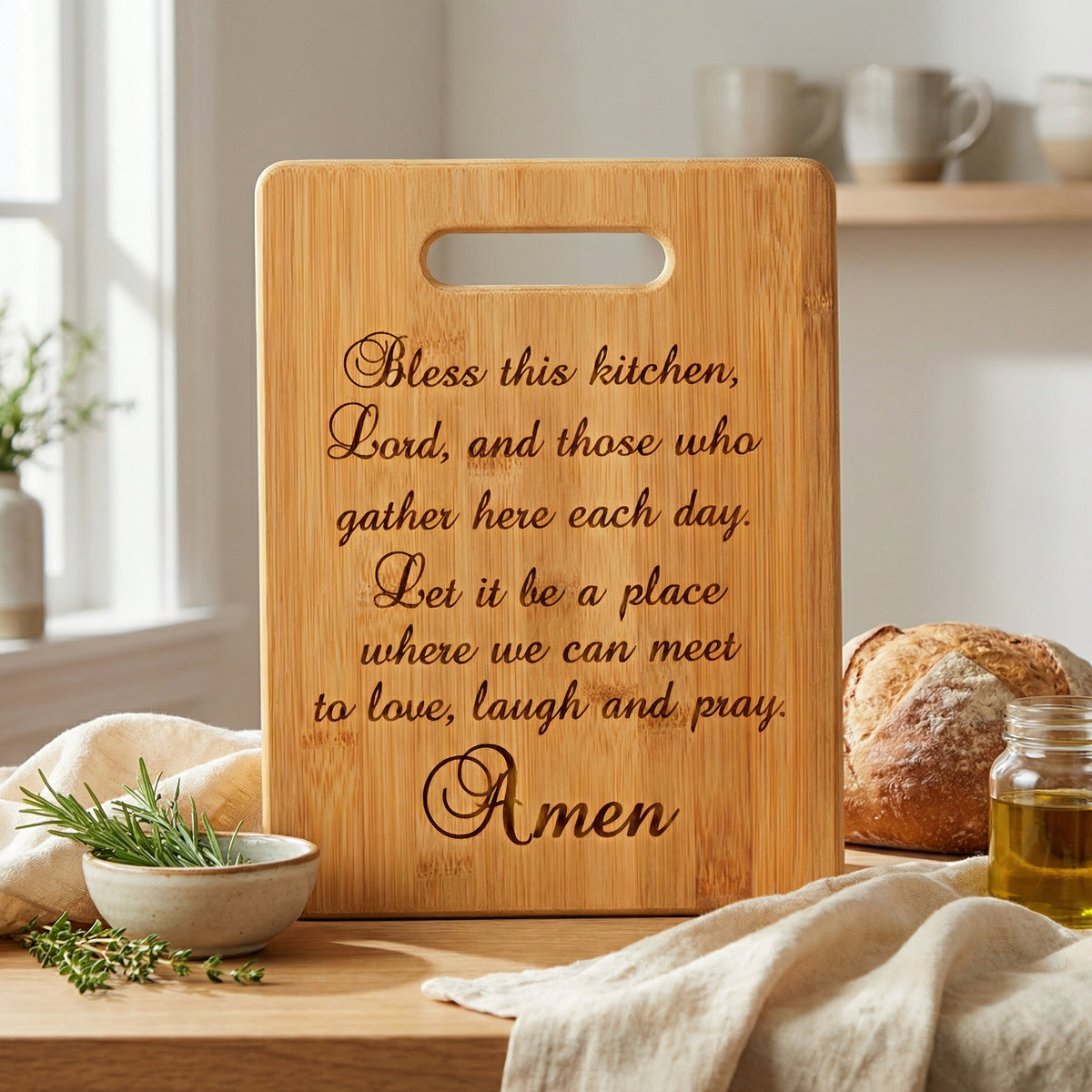A wooden cutting board with a prayer message engraved on it, placed on a kitchen counter with various kitchen items such as a loaf of bread, a jar of oil, and a bowl of herbs.