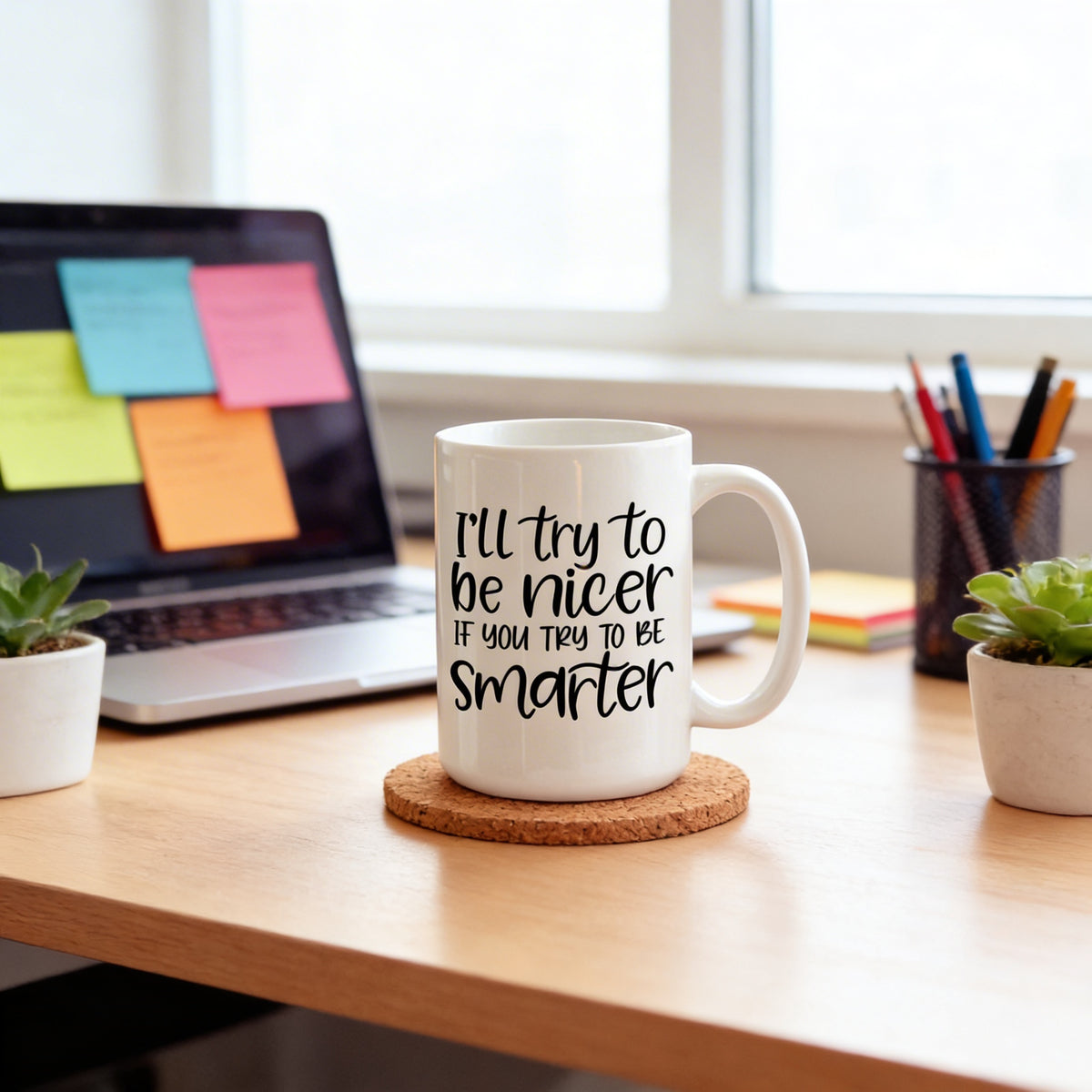 A white mug with a humorous text printed on it, placed on a cork coaster on a wooden desk. In the background, there is a laptop with sticky notes on it, and a small potted plant is visible on the desk.