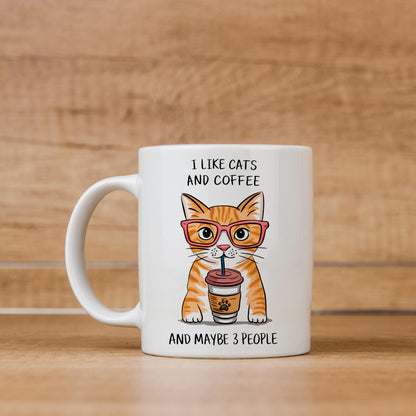 A white ceramic mug with an illustration of an orange cat wearing glasses and holding a coffee cup, accompanied by the text "I LIKE CATS AND COFFEE AND MAYBE 3 PEOPLE".