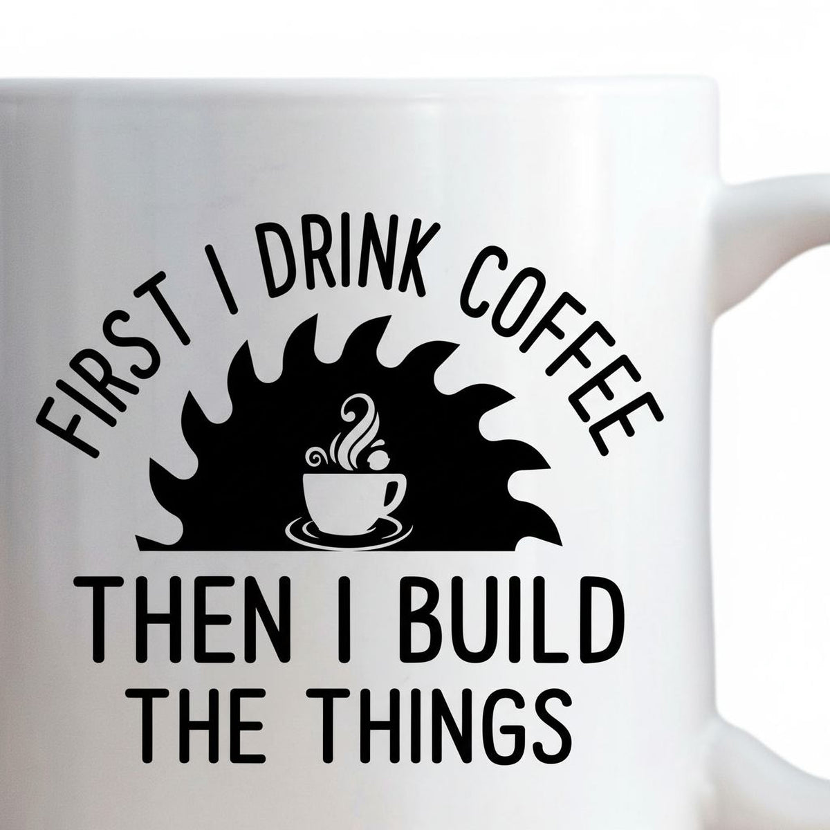 A white mug with a black and white graphic design featuring a coffee cup and a saw blade, along with the text "FIRST I DRINK COFFEE THEN I BUILD THE THINGS".
